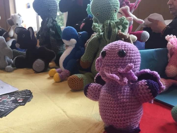 Gros plan sur un cthulhu violet, réalisé au crochet; D'autres personnages réalisés au crochet se trouvent en arrière-plan.